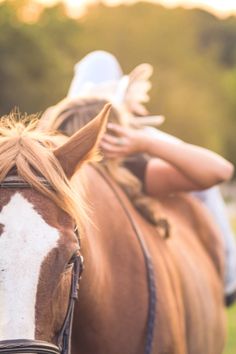 a woman riding on the back of a brown and white horse next to a lush green field