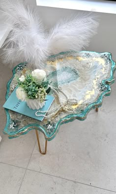 a glass tray with flowers and feathers on it sitting on a table next to a window