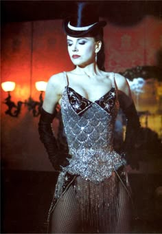 a woman wearing a top hat and dress with sequins on the skirt is standing in front of a red light