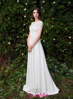 a woman standing in front of some bushes wearing a white dress and posing for the camera