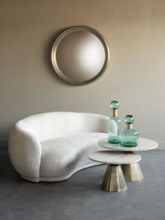 a white couch sitting next to a table on top of a gray floor under a round mirror