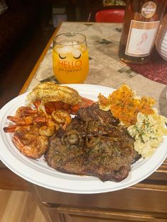 a white plate topped with steak, shrimp and other foods next to a glass of orange juice