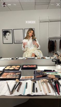 a woman sitting in front of a table filled with makeup