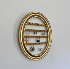 an oval gold frame holds earrings and earring hooks on a white wall behind it