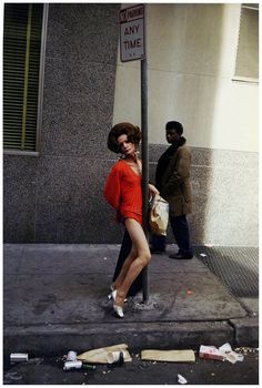 a woman in an orange dress is talking on her cell phone next to a street sign