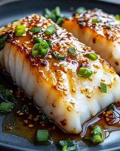 two pieces of fish on a plate covered in sauce and garnished with green onions