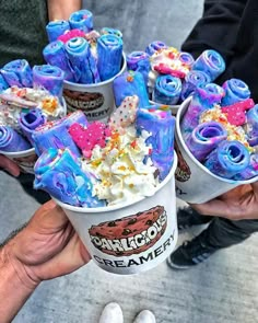 two hands holding cups filled with ice cream covered in sprinkles and candy