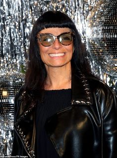 a woman wearing sunglasses standing in front of a shiny wall with silver sequins