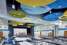 an empty classroom with blue and yellow ceilinging, tables and chairs in the middle