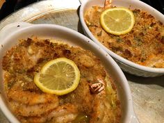 two white bowls filled with food on top of a metal tray and topped with lemon wedges