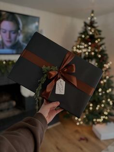 a person holding up a present in front of a christmas tree