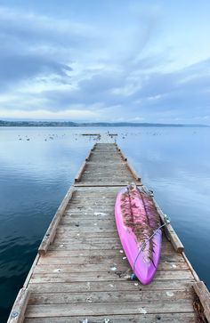 a pink surfboard sitting on top of a wooden dock