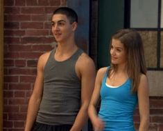 a young man and woman standing next to each other in front of a brick building