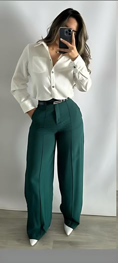 a woman is taking a selfie with her cell phone while wearing green pants and a white shirt