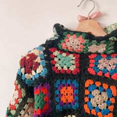 a colorful crocheted jacket hanging on a wooden hanger next to a white wall