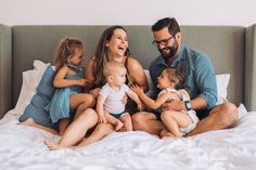 a man and two women are sitting on a bed with three children in front of them