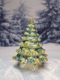 a small ceramic christmas tree sitting on top of a table next to snow covered trees