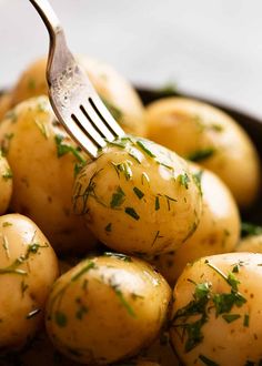 a fork picking up some potatoes with herbs on them in a black bowl next to other potatoes