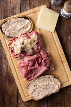 a wooden cutting board topped with meat and cheeses next to two slices of bread