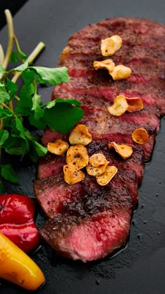 a piece of steak and some vegetables on a black surface with water droplets running down the side