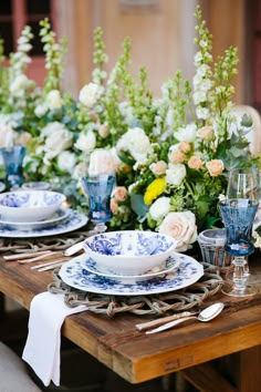 the table is set with blue and white china plates, silverware, and flowers