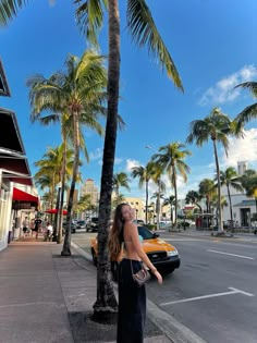 a woman standing on the side of a road next to palm trees