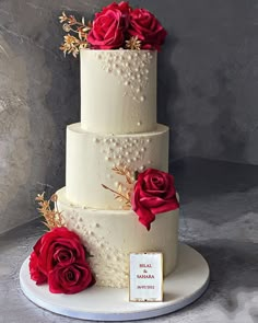 a three tiered wedding cake with red roses on top