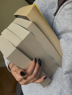 a woman holding an open book in her hands while wearing black nail polish on her nails