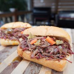 two sandwiches with meat and vegetables on a cutting board