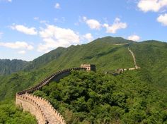 the great wall of china is surrounded by green mountains and trees, with clouds in the sky