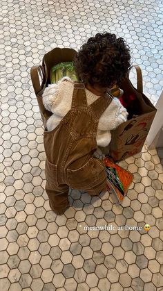 a toddler sitting on the floor with a teddy bear in a bag