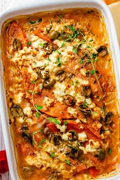 a casserole dish with tomatoes, olives, cheese and herbs on top