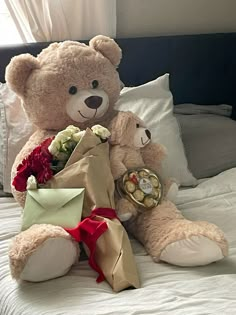 a teddy bear sitting on top of a bed next to a bouquet of flowers and an envelope