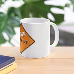 a white coffee mug sitting on top of a wooden table next to a blue book