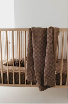 a baby crib with two brown blankets hanging from it's rails and another blanket on top of the crib