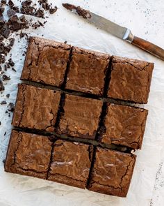 chocolate brownies cut into squares on top of parchment paper with a knife next to them