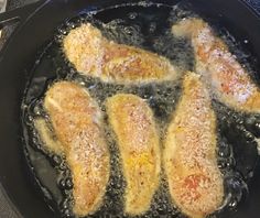 four pieces of chicken cooking in a skillet on the stove top with oil and seasoning