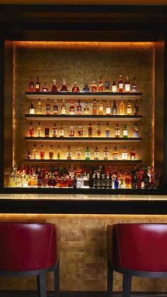 two red chairs sitting in front of a bar with bottles on the wall behind it