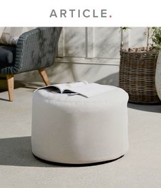 a white ottoman sitting on top of a cement floor next to a wicker basket