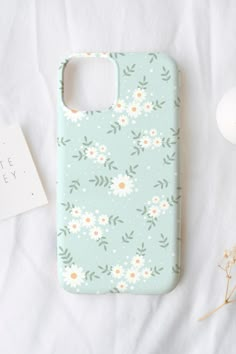 a phone case sitting on top of a bed next to a flowery plant and an egg