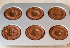 a muffin tin filled with chocolate cupcakes on top of a marble counter