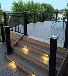 some lights are lit up on the steps in front of a deck that is surrounded by trees