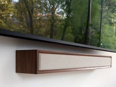 a wall mounted speaker sitting on top of a wooden shelf next to a large window