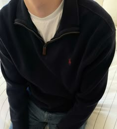 a young man sitting on top of a bed wearing a black sweater and jeans with his hands in his pockets