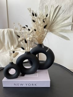 two black vases sitting on top of a table next to each other with flowers in them