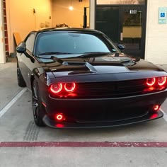 a black sports car parked in front of a building with its lights on and it's hood up