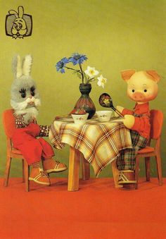 two stuffed animals sitting at a table with food and flowers in front of them,