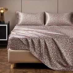 a bed with a leopard print comforter and two pillows on top of it, next to a night stand