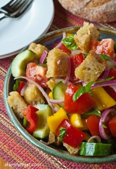 a colorful salad is in a bowl on a table next to a plate with bread