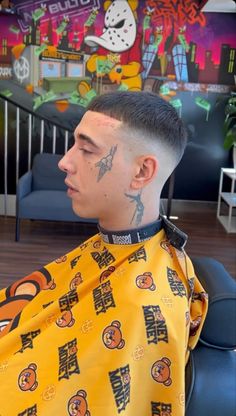 a man with a tattoo on his head sitting in a barbershop wearing a yellow shirt